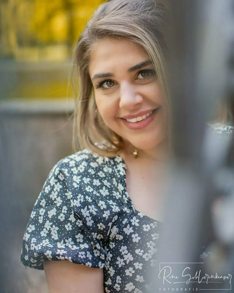 Strahlendes Portrait einer Frau im geblümten Kleid vor herbstlichem Hintergrund
