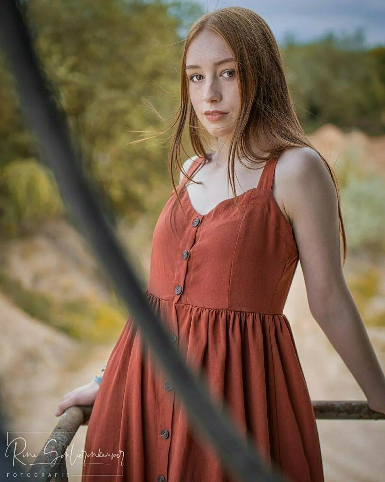 Portrait einer jungen Frau im rostroten Sommerkleid an einem alten Geländer