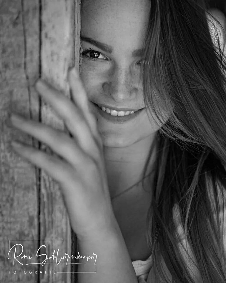 Schwarzweiß-Portrait einer lachenden jungen Frau an einer verwitterten Holzwand
